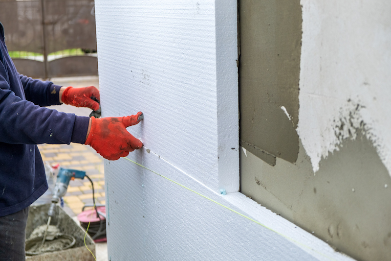 Construction worker installing styrofoam insulation sheets on house facade wall for thermal protection.