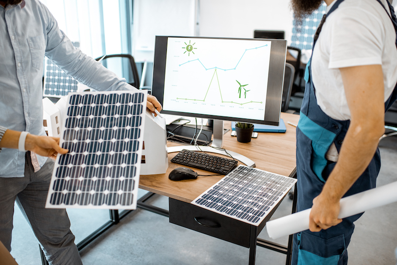 People working on a project of alternative energy, working with house model and computer in the office, close-up on the working place